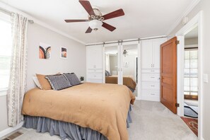 Ein Schlafzimmer mit Bett, Deckenventilator, Kleiderschrank und einer Tür zu einem weiteren Raum.