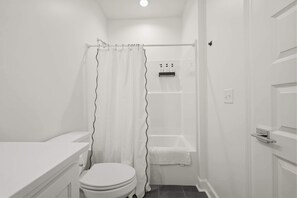 Ein kleines, weißes Badezimmer mit Toilette, einer Duschvorhang, einer Badewanne und einem weißen Handtuchhalter.