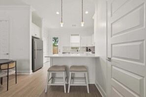 A modern kitchen with white cabinetry, a stainless steel refrigerator, two bar stools, and pendant lighting. - Kali House •  River Ranch • Prime Location • Premier Host (Lafayette)