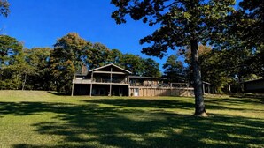 A two-story building with a large porch and a covered outdoor area, surrounded by trees and grass.