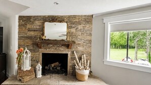 A living room with a stone fireplace, a large window, and a television.