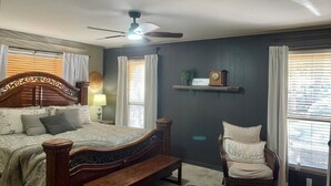A bedroom with a wooden bed, a bench, a chair, a ceiling fan, and a shelf with a clock. - 2 Story lakefront home- on the Narrow's of Greers Ferry Lake (Greers Ferry)