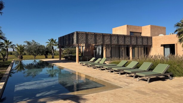 Zona de piscina amb gandules, una piscina cristal·lina i un edifici de disseny modern.