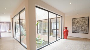 Una habitació àmplia amb grans portes de vidre que donen a zona exterior, un vas vermell i una obra d'art emmarcada a la paret.