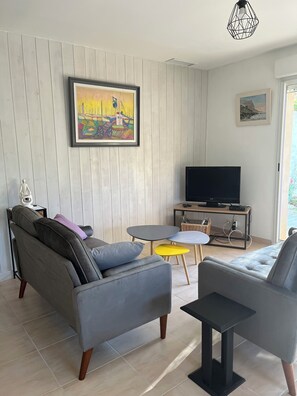 A living room with a sofa, armchair, TV, and a painting on the wall.