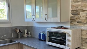 Eine Küche mit hellen Holzschränken, einem Einbauofen, einem Toaster und einem Fenster mit Blick ins Grüne.
