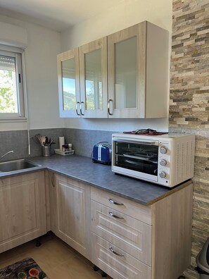 A kitchen with light wood cabinets, a built-in oven, a toaster, and a window with a view of greenery.
