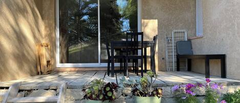 A patio with a sliding glass door, a wooden chair, a table, and potted plants.