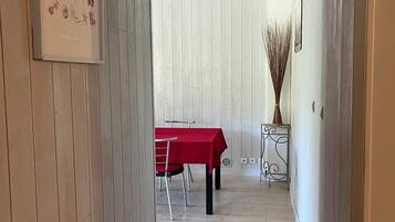 Een gang met een eethoek, met een rode tafel en stoelen, een ingelijst beeld aan de muur, en een vaas met hoge planten.