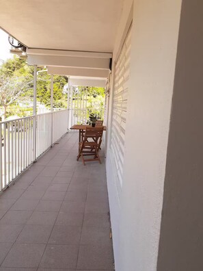 Ein überdachter Balkon mit Tisch und Stühlen, weißen Geländern und Blick ins Grüne.
