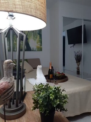 Ein Zimmer mit einem Bett, einem Tisch mit Flasche und Gläsern, einer Lampe, einem Gemälde und einem Fernseher an der Wand.