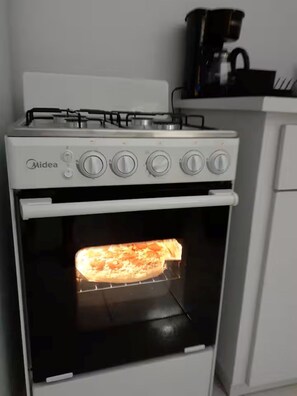 Eine Küche mit Herd und Backofen, eine Pizza im Backofen und eine Kaffeemaschine auf der Arbeitsfläche.