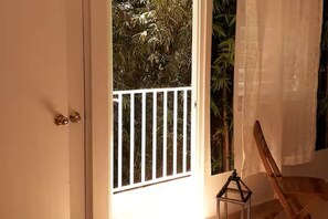 Ein Zimmer mit einer Tür, einem Fenster mit Blick auf Grünpflanzen und einem kleinen Tisch mit einer Laterne.