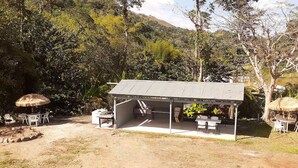 Una pequeña estructura al aire libre con techo de metal, rodeada de vegetación natural y un sendero de tierra.