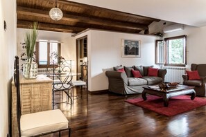 Ein Wohnzimmer mit Holzboden, einer Sofagarnitur, einem Couchtisch und einem Essbereich mit einem Stuhl und einer Pflanzenvase.
