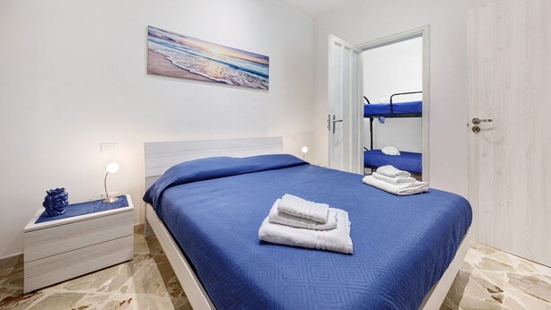 Un dormitorio con cama, una mesita de noche, una lámpara de noche, un cuadro en la pared y una puerta que da a otra habitación.