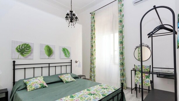 Ein Schlafzimmer mit einem Bett, einem Hängestuhl, einem kleinen Tisch, einem Spiegel und einer Chandelier.