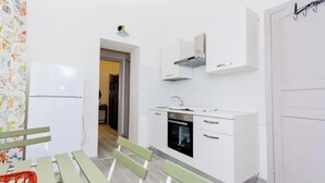 Eine kompakte Küche mit weißen Schränken, einem eingebauten Backofen und einem Spülbecken. Eine Tür mit Haken ist an der Wand, und eine grüne Sitzbank mit Korb steht dort.