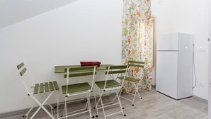 Eine kleine Küchenzeile mit einem weißen Kühlschrank, einem Esstisch mit grünen Stühlen und einem blumigen Vorhang.
