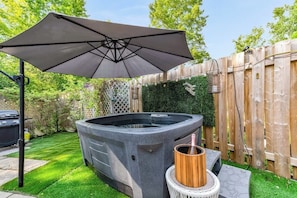 Un bain à remous avec un seau en bois, un parasol et une clôture en bois, le tout installé dans un jardin.
