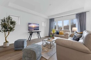 A modern living room with a sofa, ottoman, coffee table, and a potted plant. - Near Niagara Falls+Wine Country+Games Tables (Thorold)