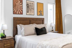 A neatly made bed with a wooden headboard, two bedside tables with lamps, and three framed pictures on the wall. - Near Niagara Falls+Wine Country+Games Tables (Thorold)