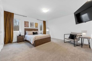 Ett modernt hotellrum med en säng, sängbord, en soffa, en tv och konstverk på väggen.