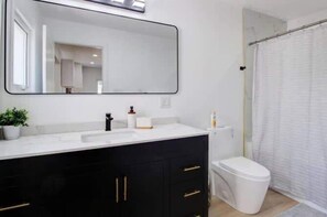 A bathroom with a white sink, black cabinets, a large mirror, and a shower curtain.