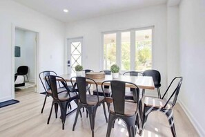 A modern dining area with a wooden table and black chairs, a potted plant, and a view of the outdoors through large windows.