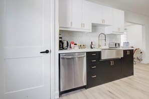 A modern kitchen with white cabinets, a stainless steel dishwasher, and a black countertop. - 5 Bedroom Island House perfect for large groups (Port Colborne)