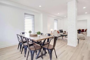 A modern dining area with a wooden table and metal chairs, a white brick column, and a seating area with a sofa and chairs. - 5 Bedroom Island House perfect for large groups (Port Colborne)