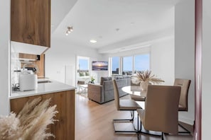 A modern kitchen with a dining area, a sofa, and a large window with a city view. - 2 BR Apartment at Station Park with Swim Spa (Kitchener)