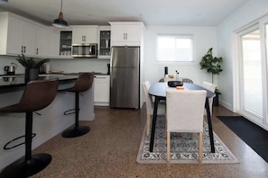 Una cocina moderna con armarios blancos, un refrigerador de acero inoxidable y un comedor con mesa y sillas.