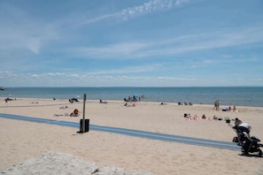 Ein Strand mit badenden Personen, einem Rettungsturm und blauem Himmel.