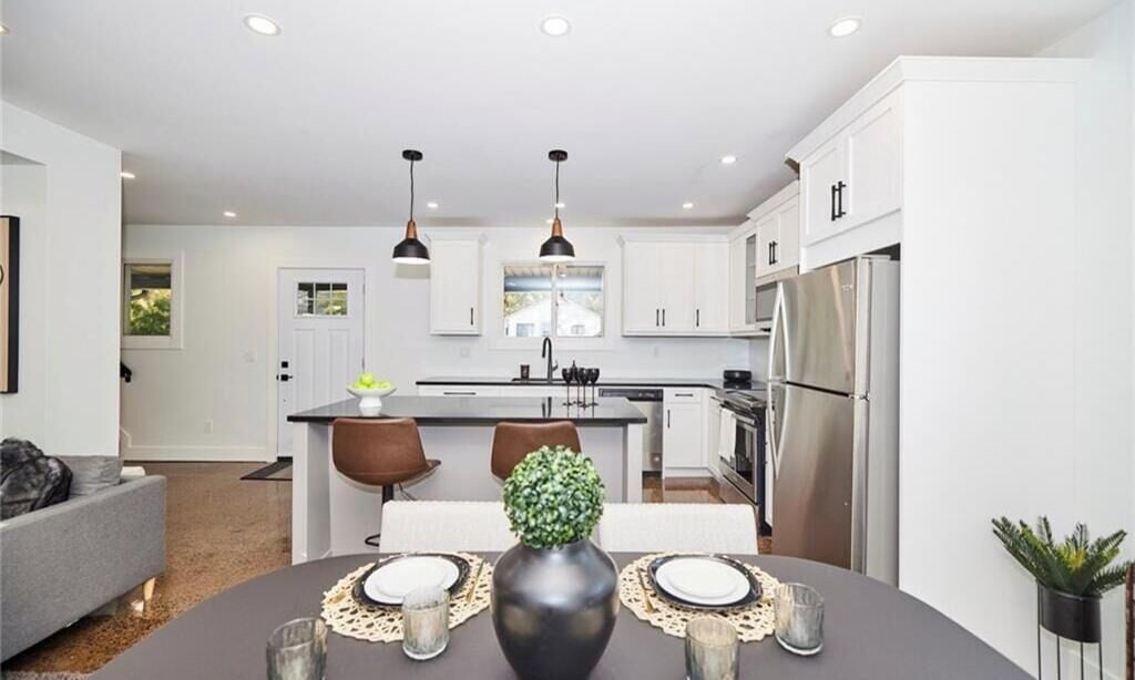 A modern kitchen with white cabinets, stainless steel appliances, pendant lighting, and a dining area with a table set for two.