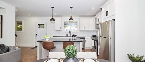 A modern kitchen with white cabinets, stainless steel appliances, pendant lighting, and a dining area with a table set for two.