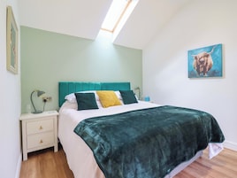 Un dormitorio con cabecera color turquesa, juego de almohadas verde y amarillo, edredón blanco y manta verde.
