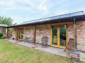 A stone building with a covered patio, outdoor seating, and a large sliding glass door. - Henlle Home Farm (Oswestry)