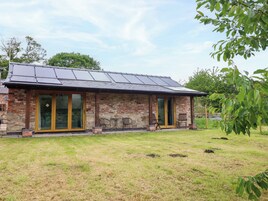 Un edificio de ladrillo con puerta de vidrio, un patio con mesas al aire libre y un techo con paneles solares.