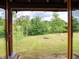 Una construcción de madera con una puerta que da a un espacio exterior cubierto de césped, árboles y una valla.