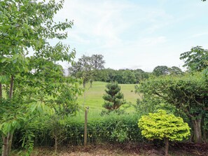 A fenced garden with various trees and shrubs, a clear sky, and a grassy field in the background. - Henlle Home Farm (Oswestry)