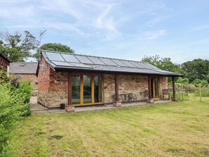 A brick building with a sloped roof, large glass doors, and a patio area with outdoor seating. - Henlle Home Farm (Oswestry)