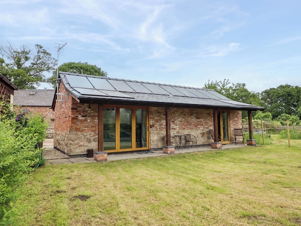 A brick building with a sloped roof, large glass doors, and a patio area with outdoor seating. - Henlle Home Farm (Oswestry)