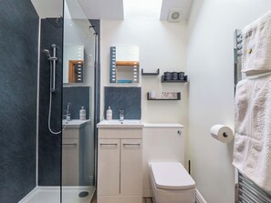 A modern bathroom with a glass-enclosed shower, a toilet, a sink with a mirror, and a shelf with toiletries. - Henlle Home Farm (Oswestry)