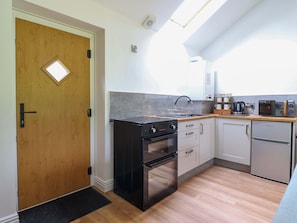 A compact kitchen with a wooden door, a black stove, a sink, and a compact refrigerator. - Henlle Home Farm (Oswestry)