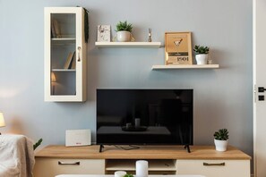 Ein modernes Wohnzimmer mit Fernseher, Holztisch und Regalen mit Dekorationselementen.