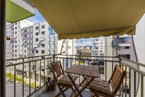Ein Balkon mit Tisch und Stühlen, Blick auf umliegende Gebäude und einem großen Sonnenschirm.