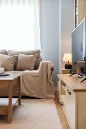 Ein Wohnzimmer mit einer Couch, einem Tisch, einer Lampe und einem Fernseher.
