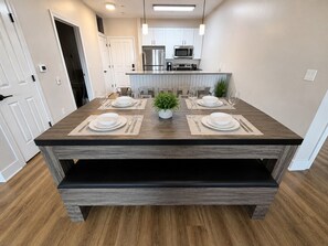 A dining area with a wooden table set for four, a kitchen in the background, and a door leading to another room. - Executive 3BR Downtown Birmingham with Game Table (Birmingham)