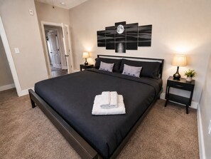 A bedroom with a large bed, two bedside tables, a wall-mounted artwork, and a door leading to another room. - Executive 3BR Downtown Birmingham with Game Table (Birmingham)